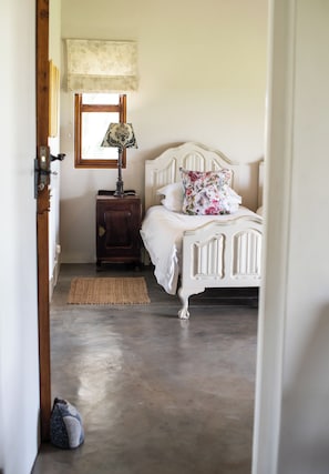 Un dormitorio con cama, mesita de noche, lámpara y ventana.