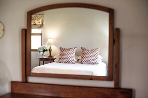 A bed with a wooden headboard, two patterned pillows, a bedside table with a lamp, and a mirror on the wall. - Merino - 2 bedroom cottage in welcoming Stanford with stunning views and space (Hermanus)