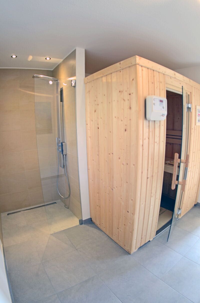 A sauna room with a wooden door, a glass shower enclosure, and a control panel.