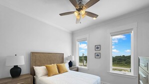 Ein Schlafzimmer mit Bett, Nachttischen, Deckenventilator und großen Fenstern.