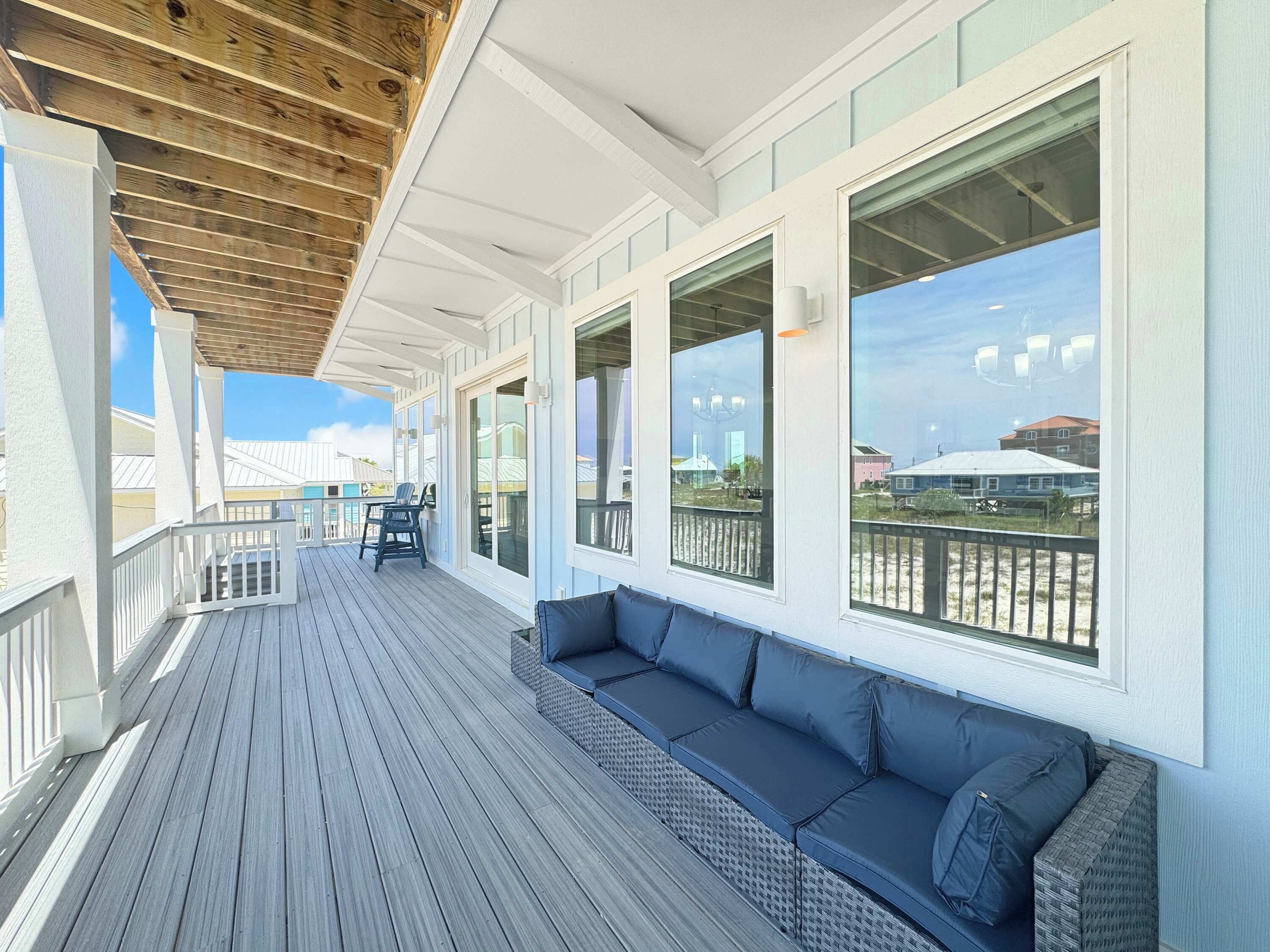 Une terrasse extérieure couverte, dotée d’un espace salon, de grandes fenêtres et offrant une vue sur la plage.