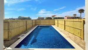Ein rechteckiger Swimmingpool, umgeben von einem Holzzaun, mit wolkenlosem, blauem Himmel.