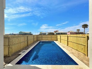 Ein rechteckiger Swimmingpool, umgeben von einem Holzzaun, mit wolkenlosem, blauem Himmel.