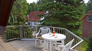Ein Balkon mit rundem Tisch, Stühlen, einer Flasche und einem Glas.