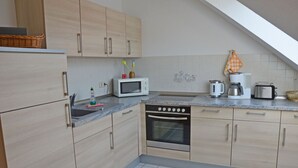 Eine kleine Küche mit hellem Holzkorpus, einer Mikrowelle, einem Backofen und einer Kaffeemaschine.