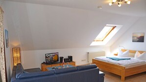 Een slaapkamer met schuine kap, een bed, een bank, een televisie en een radiator.