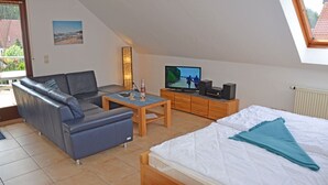 Ein gemütlicher, kleiner Wohnraum mit einer Couch, einem Bett, einem Fernseher und einem kleinen Tisch.