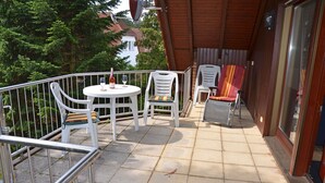 Een balkon met een ronde tafel, vier stoelen, een fles wijn en een glas op de tafel.