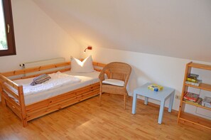 Ett litet, ombonat rum med en säng i våningssäng av trä, en flätad fåtölj, ett litet bord och en bokhylla.
