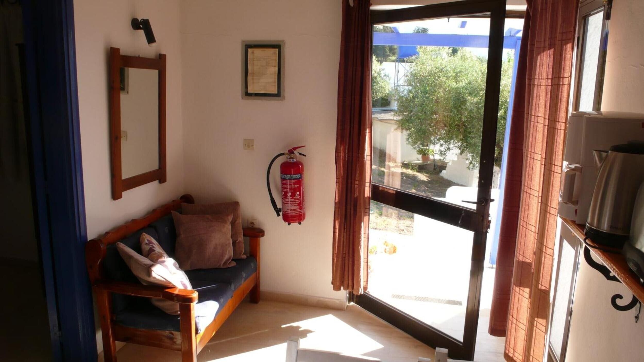 A room with a wooden bench, a fire extinguisher, a mirror, and a window with curtains.