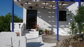 A white building with a covered porch, potted plants, and a stone wall. - Stefanos Garden Apartment with Mountain View, Wi-Fi, and Air Conditioning (Apokoronos)