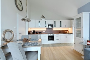 Eine moderne Küche mit weißen Schränken, einem Essbereich mit Tisch und Stühlen sowie einem eingebauten Backofen.