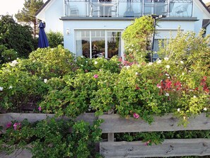Ein Haus mit Balkon, Holzzaun und verschiedenen blühenden Pflanzen.