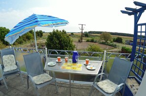A patio with a table set for two, chairs, a striped umbrella, and a view of the countryside. - Vacation rental, very quiet location, about 400 m from the sandy beach (Baltic Sea), Wi-Fi (Glowe)
