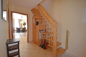 A wooden staircase leading to a second floor, a dining area with chairs and a table, and a small wooden cabinet with a red object on the floor. - Vacation rental, very quiet location, about 400 m from the sandy beach (Baltic Sea), Wi-Fi (Glowe)