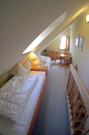 A bedroom with a sloped ceiling, a bed with white bedding, a bedside table with a lamp, and a small desk with a chair. - Vacation rental, very quiet location, about 400 m from the sandy beach (Baltic Sea), Wi-Fi (Glowe)
