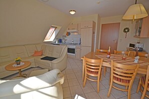 Ein gemütlicher Wohnbereich mit Sofa, Esstisch und Stühlen, einer kleinen Küchenzeile und einem Fenster mit Tageslicht.