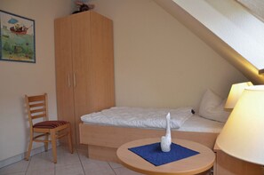 Ein kleiner, gemütlicher Raum mit einem Einzelbett, einem Holzschrank, einem Sessel und einem Tisch mit einer Dekoration.