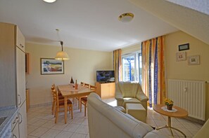 A living room with a sofa, a dining table with chairs, a television, and a window with curtains. - Vacation rental, very quiet location, about 390 m from the sandy beach (Baltic Sea), Wi-Fi (Glowe)