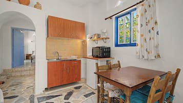 Een compacte keuken met houten kastjes, een betegelde spatwand, een magnetron en een raam met gordijnen.