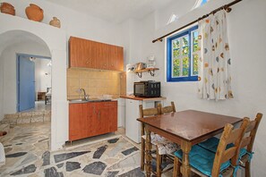 Eine kompakte Küche mit Holzausstattung, einer gefliesten Spritzschutzleiste, einer Mikrowelle und einem Fenster mit Vorhängen.