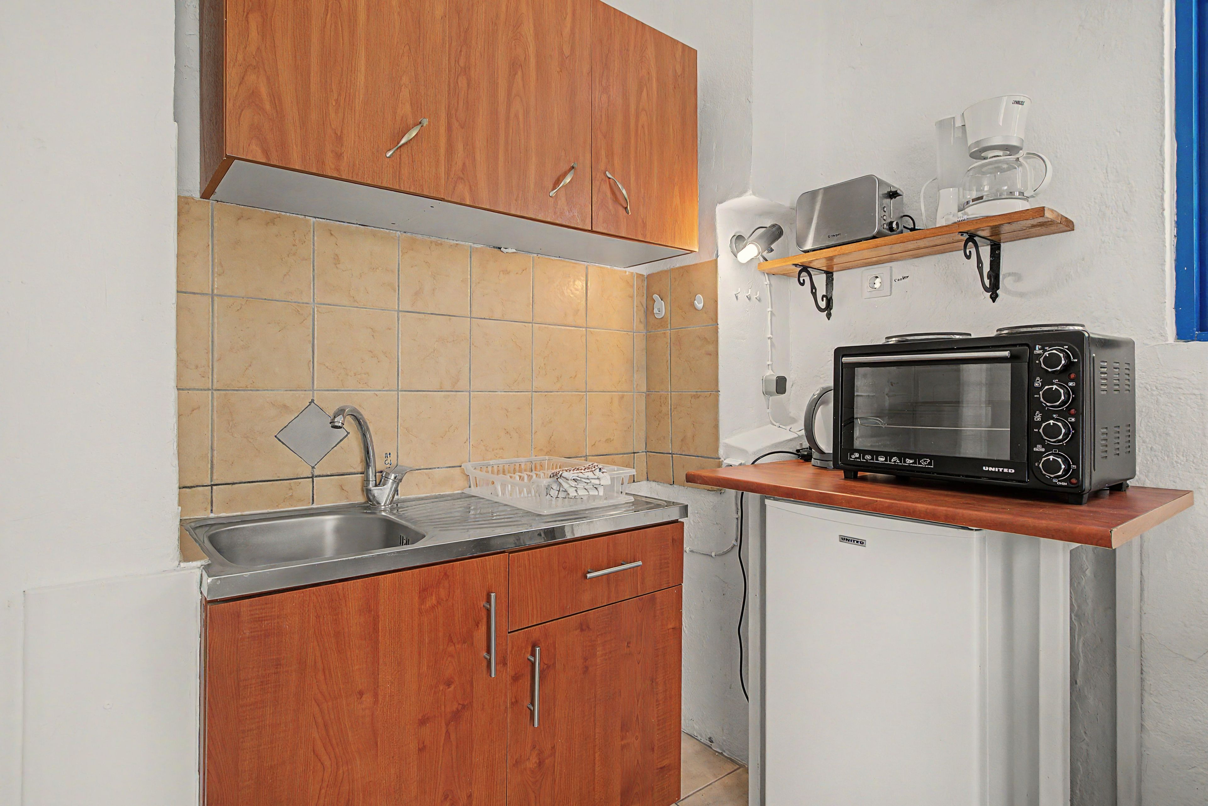 Cocina compacta con armarios de madera, un lavamanos de acero inoxidable, un microondas y una cafetera en un estante.