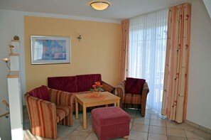A living room with a sofa set, a table with a vase of flowers, a painting on the wall, and a window with curtains. - Vacation rental, very quiet location, about 400 m from the sandy beach (Baltic Sea), Wi-Fi (Glowe)