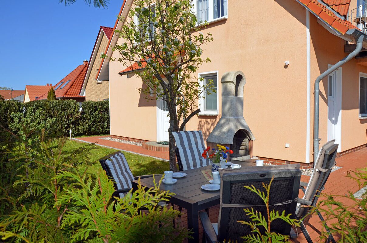 A patio with a table set for dining, a stone oven, and a tree in the background.