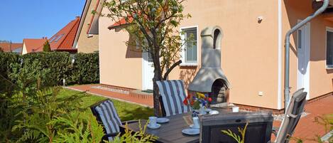 A patio with a table set for dining, a stone oven, and a tree in the background.