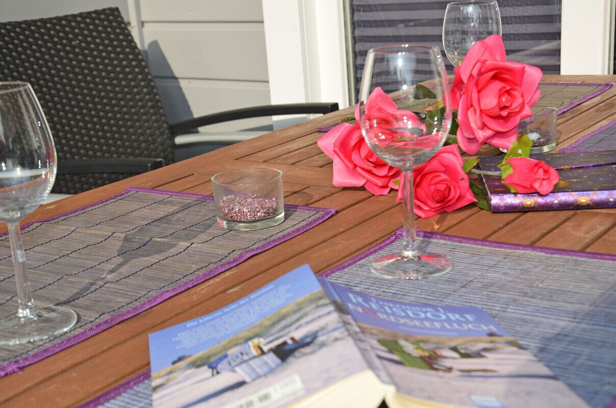 A wooden table with a placemat, two wine glasses, a small candle, and pink roses.