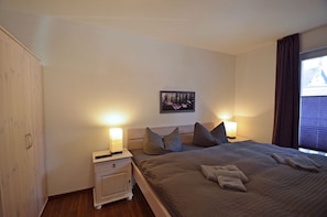 A bedroom with a bed, bedside lamps, a nightstand, a wardrobe, and a wall-mounted picture. - Just 500 meters from the sandy Baltic Sea beach, Wi-Fi, and a washing machine with a covered patio (Glowe)