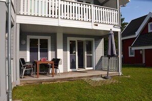 A two-story house with a covered porch, a dining table with chairs, and a patio umbrella. - Just 500 meters from the sandy Baltic Sea beach, Wi-Fi, and a washing machine with a covered patio (Glowe)