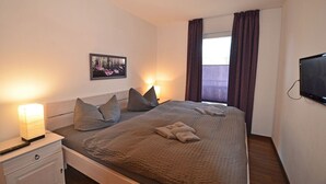 A bedroom with a bed, bedside lamps, a television, a window with curtains, and a picture on the wall. - Just 500 meters from the sandy Baltic Sea beach, Wi-Fi, and a washing machine with a covered patio (Glowe)