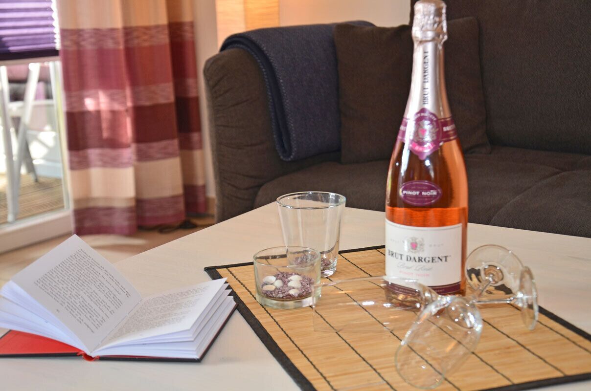 A bottle of Brut Dargent wine, two glasses, a book, and a small bowl with nuts on a table.
