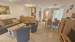 A modern living room with a sofa, coffee table, and armchairs, a dining area with a table and chairs, and a kitchen in the background. - Just 400 meters from the sandy Baltic Sea beach, Wi-Fi, and a washing machine with a covered patio (Glowe)
