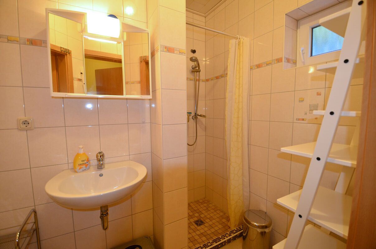 Ein Badezimmer mit Waschbecken, Spiegel, Dusche und einer Leiter.