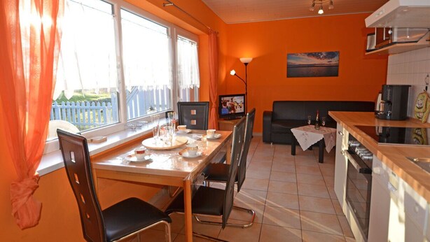 Een eetgedeelte met een tafel voor twee personen, een bank en een keuken voorzien van apparatuur.