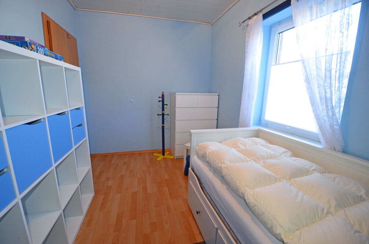 Ein Schlafzimmer mit Bett, Kleiderschrank, Fenster und Regalelement.