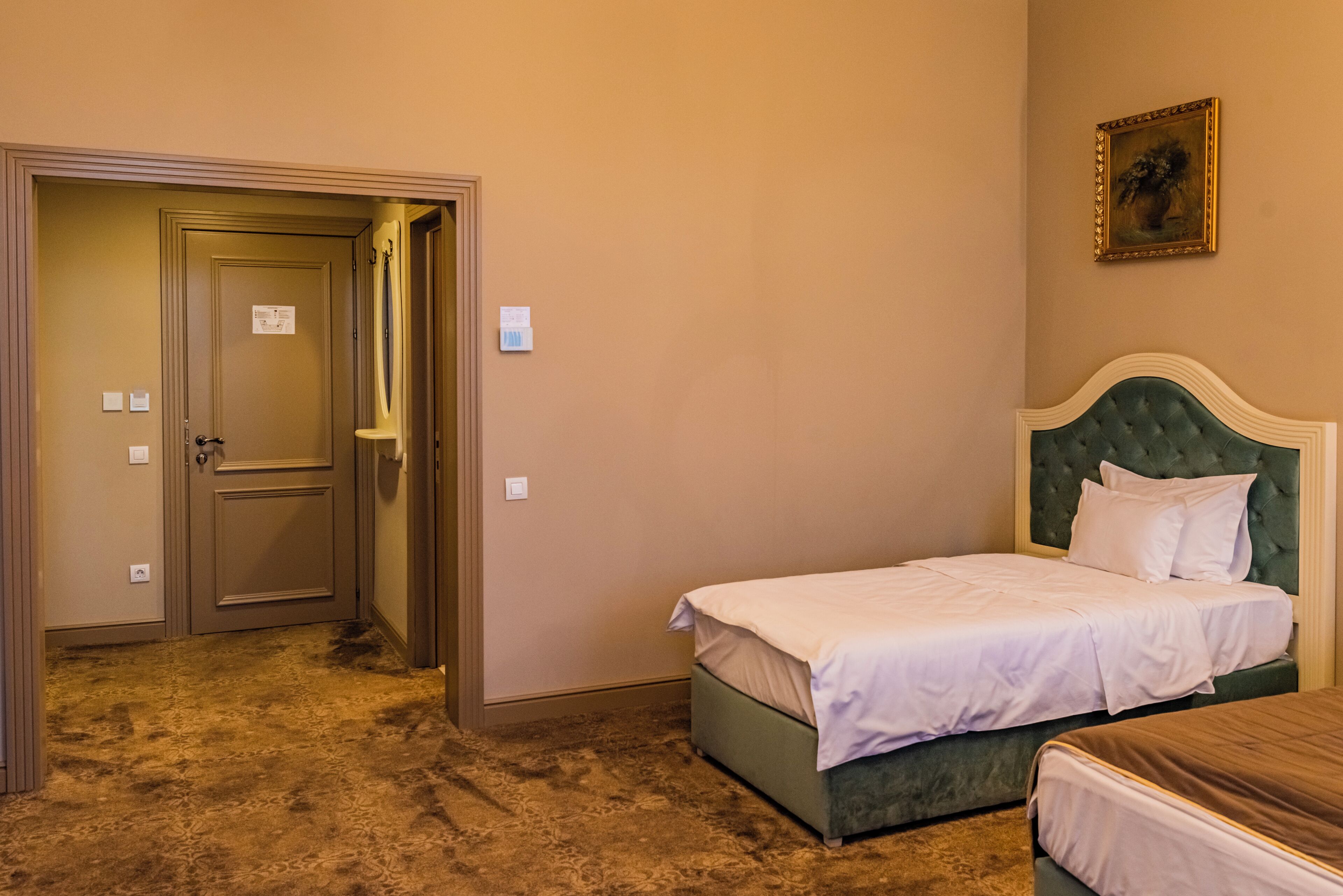 Quarto de hotel com cama de casal, cabeceira estofada em verde, mesinha de cabeceira e porta de acesso a um banheiro.