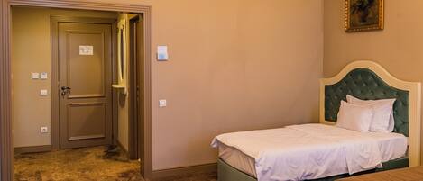 Quarto de hotel com cama de casal, cabeceira estofada em verde, mesinha de cabeceira e porta de acesso a um banheiro.