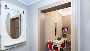 A hotel room with a large mirror, a television, a desk with a vase of flowers, and two red chairs. - Grand Hotel Traian (Iași)