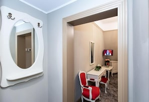 A hotel room with a large mirror, a television, a desk with a vase of flowers, and two red chairs. - Grand Hotel Traian (Iași)