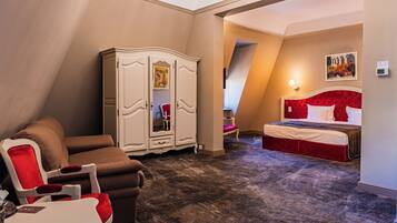 A hotel room with a red bed, a brown sofa, a white wardrobe, and a red armchair.