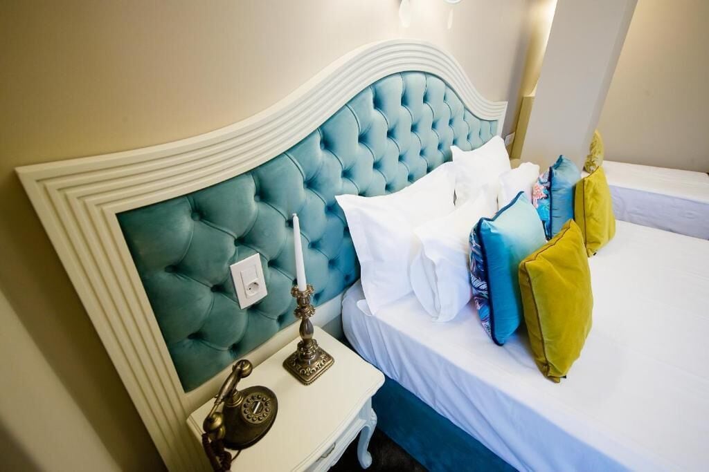 A hotel room with a tufted headboard, a bedside table with a lamp, and a bed with multiple pillows.