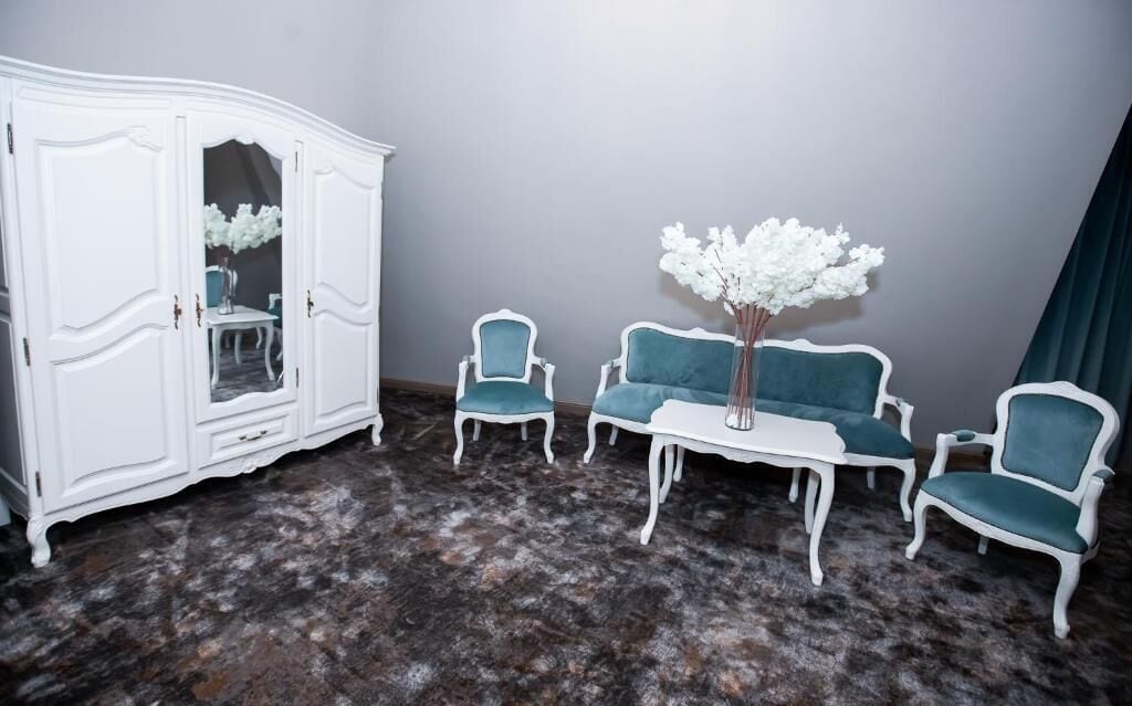 A room with a white wardrobe, two teal armchairs, a small white table, and a vase with white flowers.
