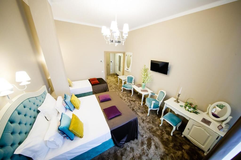 A hotel room with a bed, a desk, a chair, a TV, and a chandelier.