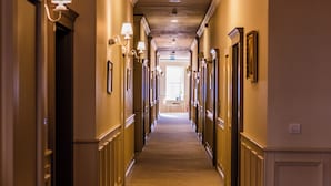 Un pasillo de hotel con puertas a ambos lados, piso alfombrado y lámparas en la pared.
