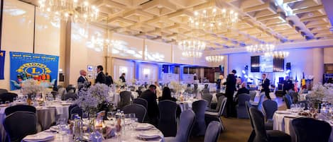 A banquet hall with round tables set for dining, chandeliers, and a stage with musical equipment.
