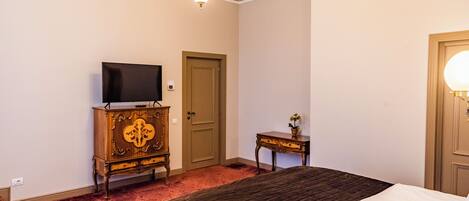 Une chambre d’hôtel avec un lit, un téléviseur posé sur une commode en bois, une porte et une petite table sur laquelle se trouve une plante.