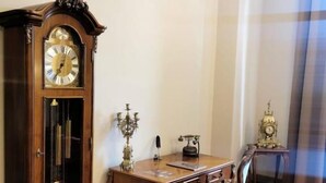 A room with a wooden desk, a chair, a large wall clock, and a window with curtains. - Grand Hotel Traian (Iași)